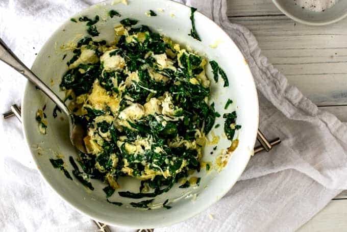 Spinach mixture and cheeses are being combined in a small white bowl.