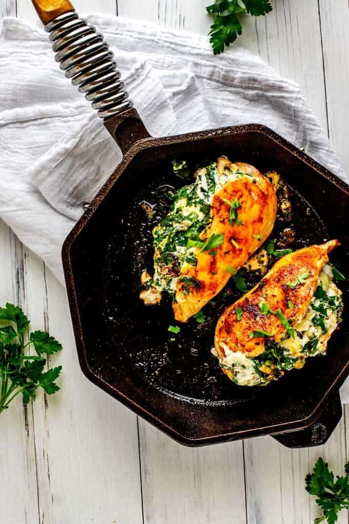 Photo of two pieces of Keto Stuffed Chicken in a cast iron skillet against a white background.