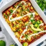 Photo of Zucchini Enchiladas in a white casserole dish garnished with sour cream and jalapeno.