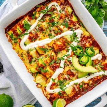 Photo of Zucchini Enchiladas in a white casserole dish garnished with sour cream and jalapeno.