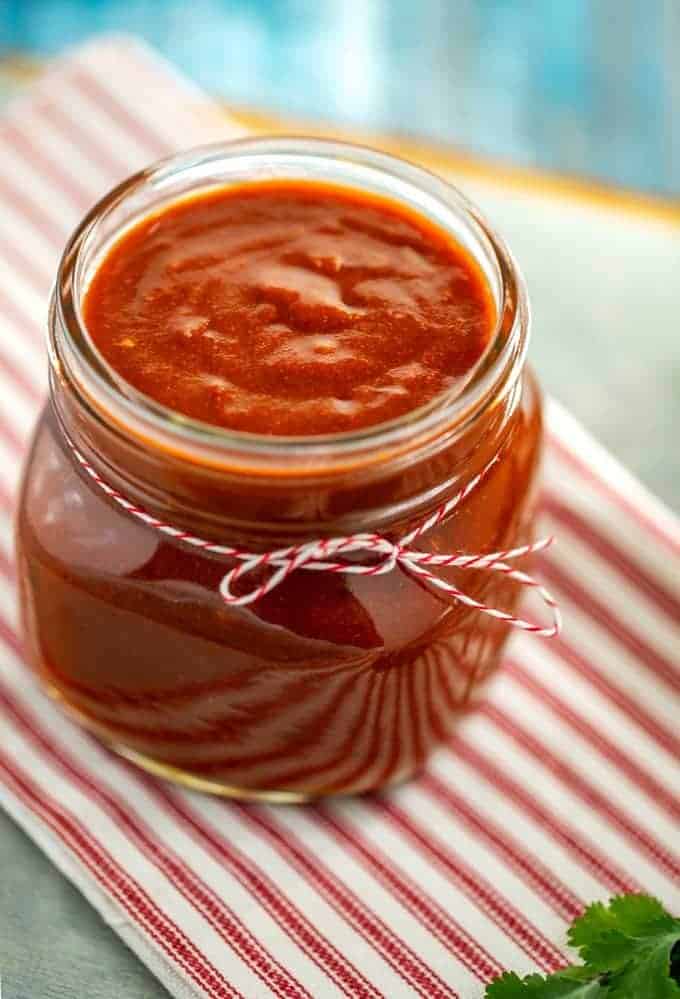 Photo of Keto Enchilada Sauce in a small glass jar with a red and white string tied around it.
