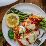 Close up overhead photo of Keto Chicken Parmesan on a white plate with asparagus and a lemon slice.