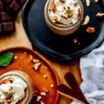 Photo of two small pots of Keto Chocolate pudding garnished with whipped cream and pecans sitting on dark wooden plates.
