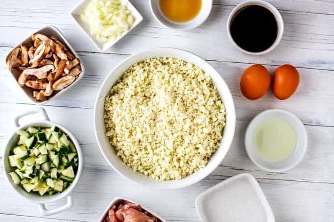 Photo of the riced cauliflower, chicken, eggs, sesame oil, avocado oil, diced onion, zucchini, mushrooms, coconut milk, and coconut aminos in white prep bowls.