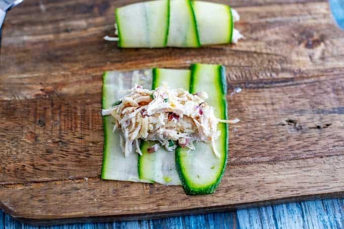 Photo of Zucchini slices with chicken on top of it sitting on a wooden cutting board.