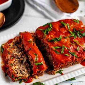 Photo of Keto Meatloaf on a white platter garnished with parsley sitting on a white background.