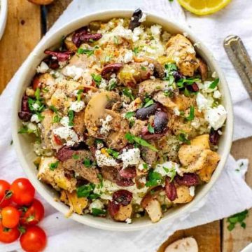 Close up overhead photo of Instant Pot Chicken and Mushrooms in a bowl sitting on a white napkin surrounded by cherry tomatoes, fresh mushrooms, olives, parsley and lemon.