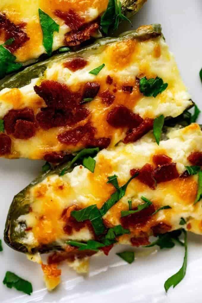 Close up photo of Low Carb Jalapeno Poppers on a white platter with bacon on top and garnished with parsley.