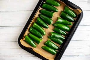Photo of jalapeños cut in half face down on a parchment lined baking sheet.