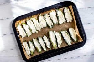 Photo of jalapenos on a parchment lined baking sheet stuffed with a goat cheese cream cheese mixture.