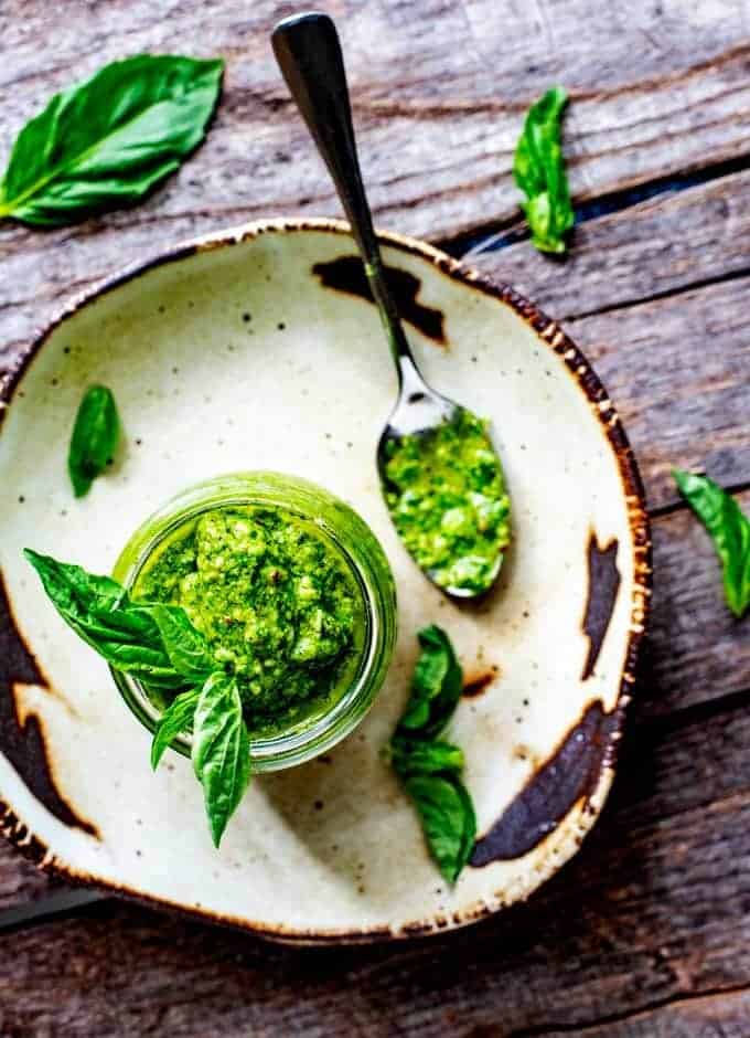 Overheat photo of Keto Pesto sitting on a rustic plate garnished with basil with a spoon sitting beside it.