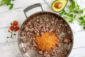 Photo of taco seasoning being added to a skillet of browned ground beef.