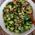Overhead photo of a Low Carb Broccoli Salad in a white mixing bowl with a wooden spoon in it sitting on a wooden background.