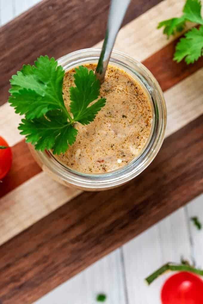Overhead photo of Tex Mex Dressing in a small glass jar with cilantro in it and cherry tomatoes next to it.