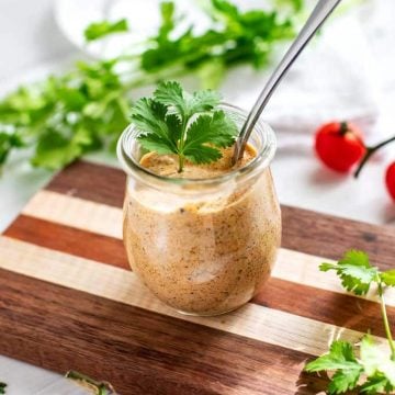 Tex Mex dressing in a small glass jar with a spoon it is and cilantro on top and scattered around it.