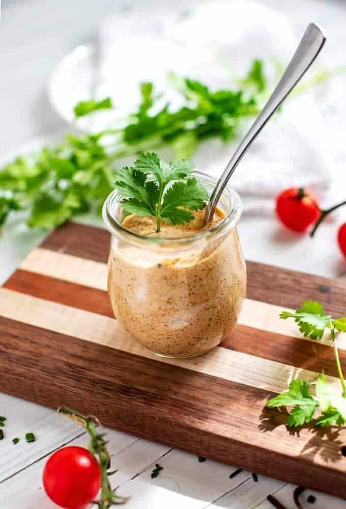 Tex Mex dressing in a small glass jar with a spoon it is and cilantro on top and scattered around it.