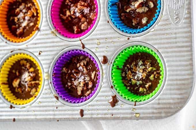 Photo of Keto Peanut Butter Cups topped with sea salt and pecans in a muffin tin.