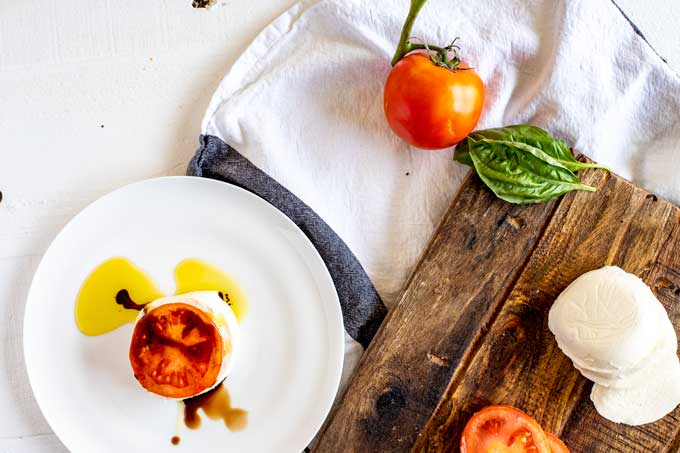Overhead photo of tomato and mozzarella drizzled with oil and balsamic vinegar.