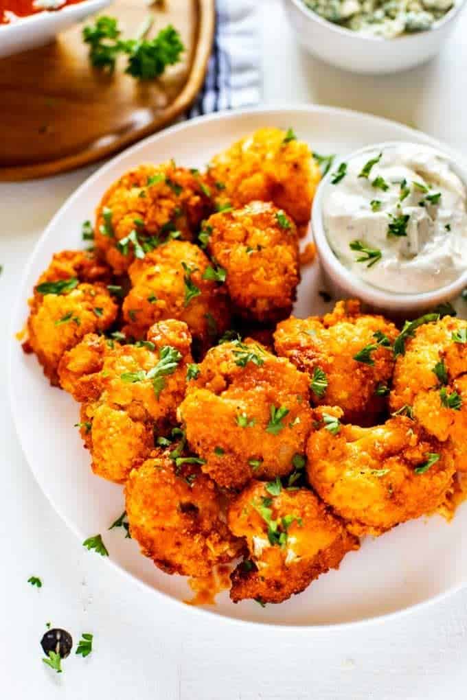 Photo of a white plate of Keto Cauliflower wings with Ranch dressing garnished with parsley.