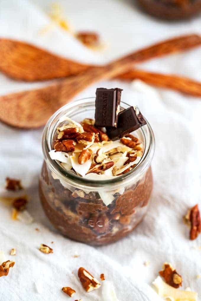 ¾ overhead photo of layered Chocolate Keto Chia Seed Pudding in a small glass bowl with coconut flakes, pecans, and chocolate sitting on a white napkin.