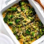 Overhead photo of Keto Chicken Broccoli Casserole in a white casserole dish with a wooden spoon on one side and plates on the other side.