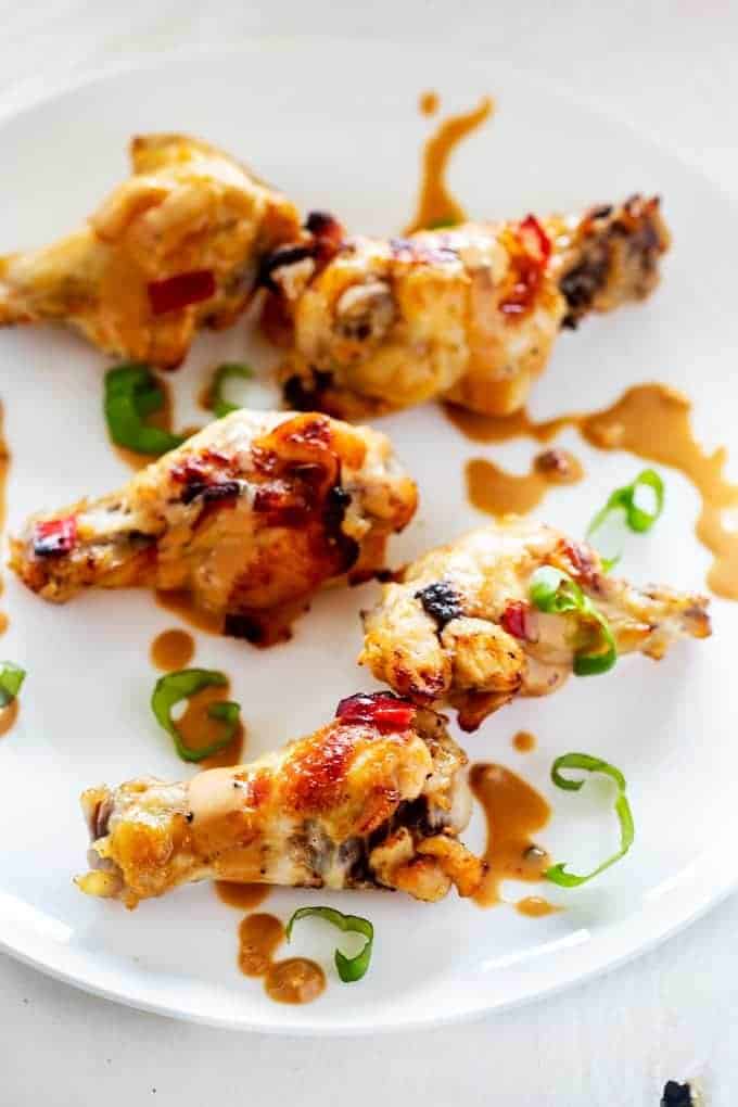 Overhead photo of Keto Chicken Wings on a white plate garnished with peanut sauce and Thai Basil.