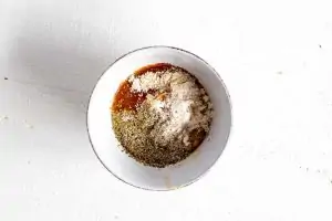 Photo of mayonaise and seasonings in a small white bowl against a white background.