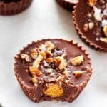 Close up photo of a Keto Peanut Butter Cup with a bite out of it with two peanut butter cups beside it and three stacked behind.
