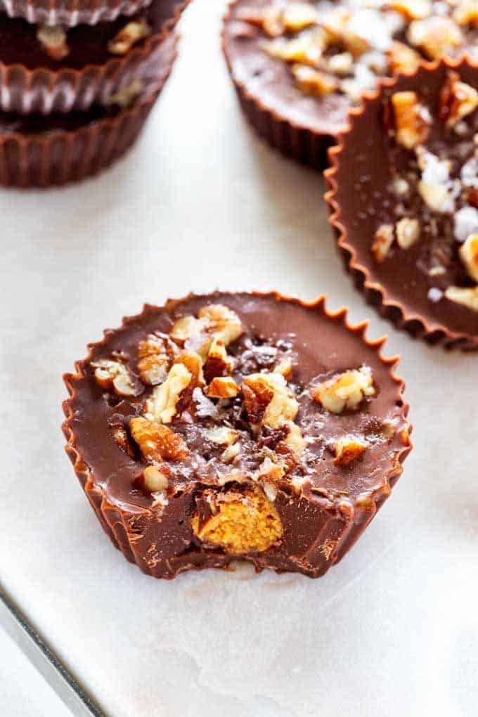 Close up photo of a Keto Peanut Butter Cup with a bite out of it with two peanut butter cups beside it and three stacked behind.