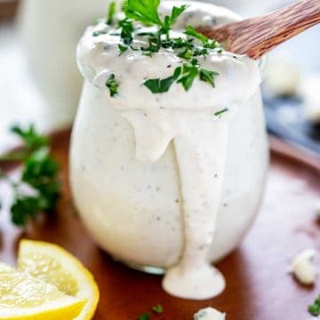 Side photo of Keto Blue Cheese Dressing in a small glass jar sitting on a wooden plate garnished with parsley.
