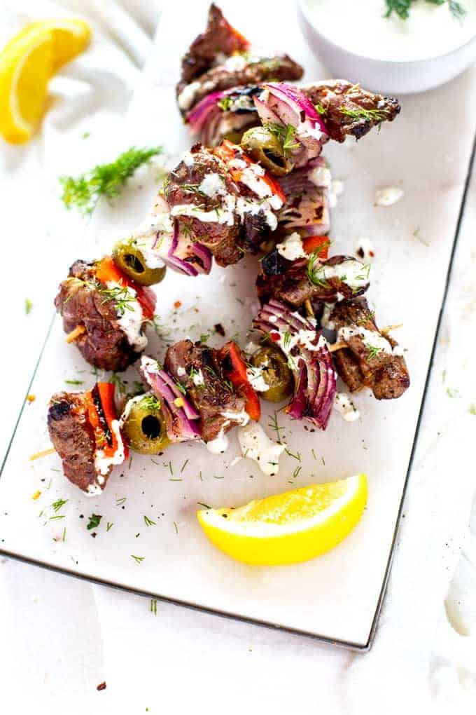 Overhead photo of Keto Lamb Kebabs on a white marble cutting board drizzles with a cream sauce and garnished with dill.