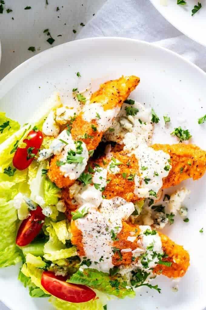 Overhead photo of Keto Buffalo Chicken on a white plate sitting on a bed of lettuces and drizzled with blue cheese dressing.