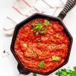 Overhead photo of Keto Marinara Sauce in a cast iron skillet garnished with parsley and sitting on a white background.