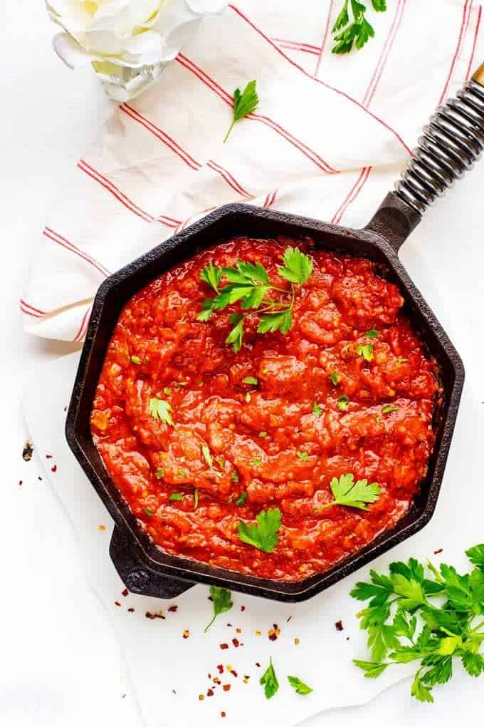 Overhead photo of Keto Marinara in a cast iron skillet garnished with parsley sitting on a white background.