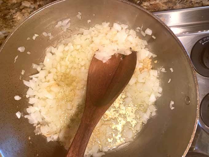 Photo of oil, chopped onion, and garlic cooking in a skillet.