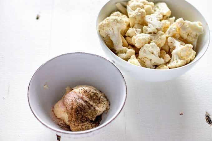Photo of cauliflower florets in a white bowl with a smaller bowl next to it that has mayonnaise, dijon mustard, and seasonings.