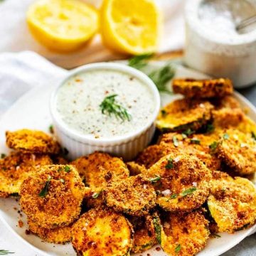 Photo of a plate of Keto Zucchini Chips with dipping sauce garnished with dill.