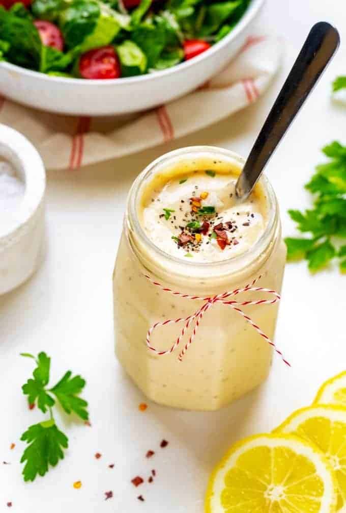 Photo of Keto Caesar Dressing in a glass jar with a spoon in it and lemons next to it.