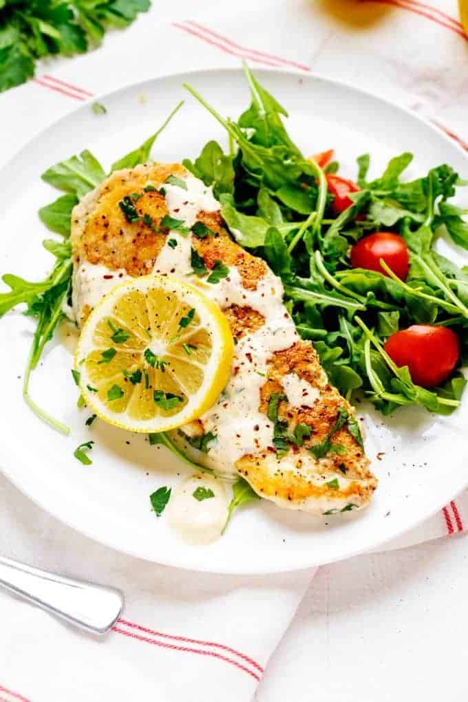 Photo of a piece of creamy Keto Lemon Chicken drizzled with lemon sauce and served over a bed of arugula.