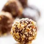 Horizontal image of Keto Truffles covered in pecans on a white background with other chocolate truffles behind it.