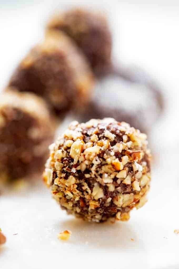 Horizontal image of Keto Truffles covered in pecans on a white background with other chocolate truffles behind it.
