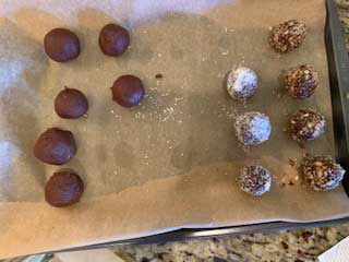 Photo of a sheet pan that has been lined with parchment paper with both rolled and unrolled chocolate truffles.