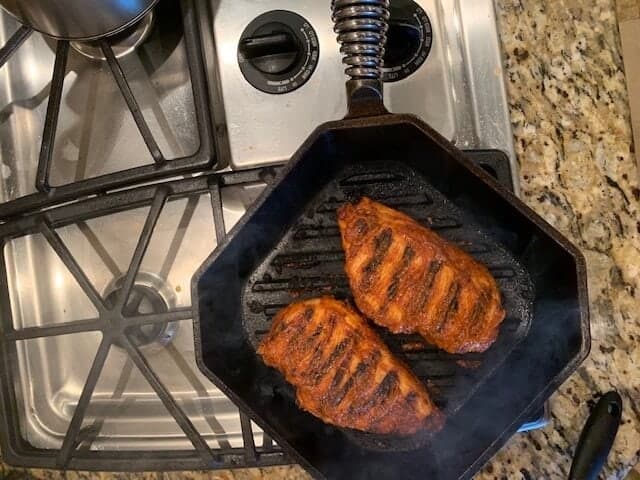 Photo of chicken in a cast iron grill pan that has been basted with BBQ sauce.