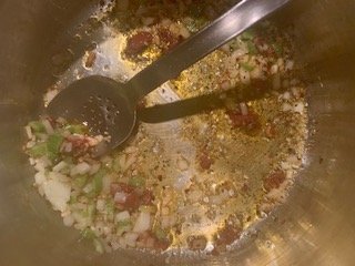 Photo of tomato paste being added to a skillet with onion, celery, and garlic.