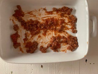Photo of meat sauce in the bottom of a casserole dish.