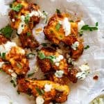 Square photo of 5 Keto buffalo wings on white parchment paper drizzled with ranch dressing and garnished with parsley.
