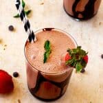 Square photo of a chocolate smoothie in a small glass garnished with chocolate, mint, and strawberries.