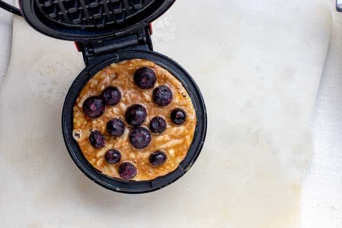 Photo of a chaffle that has been spread into a dash mini cooker with blueberries on top of it.