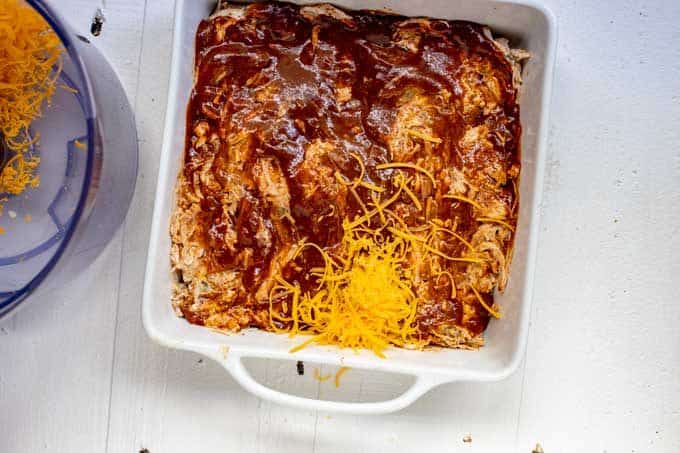Photo of a white square casserole dish with enchilada sauce poured over the filling.