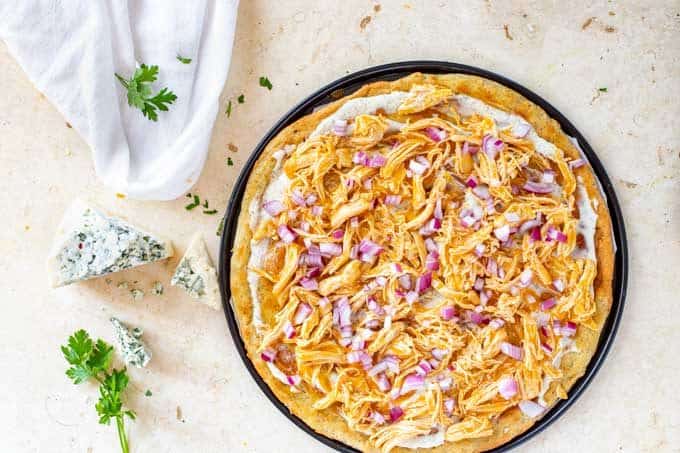 Photo of red onion and chicken on top of a ranch dressing covered pizza crust.